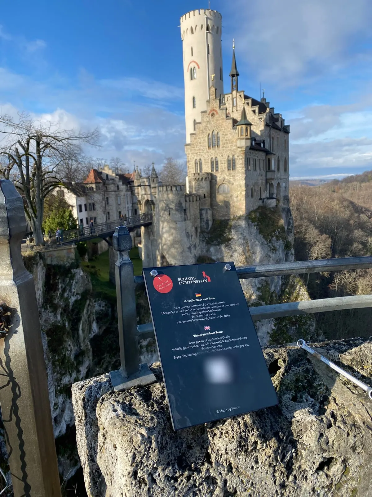 Das Schild zum virtuellen Turmausblick auf der Mauer, dahinter Schloss Lichtenstein auf seinem Felsen